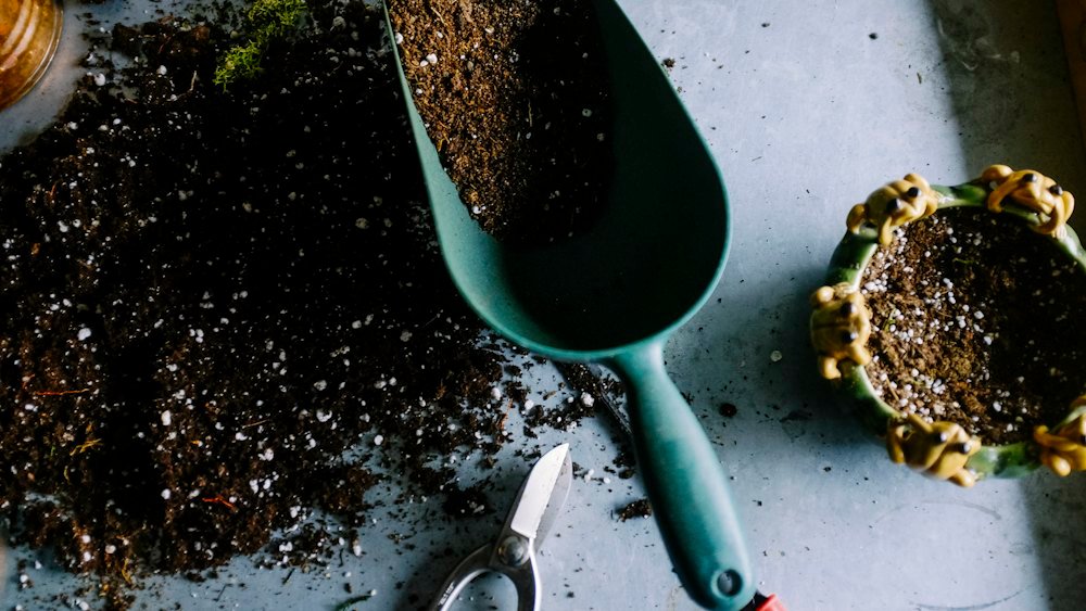 Substrato escuro espalhado sobre bancada ao lado de uma pá de jardinagem verde